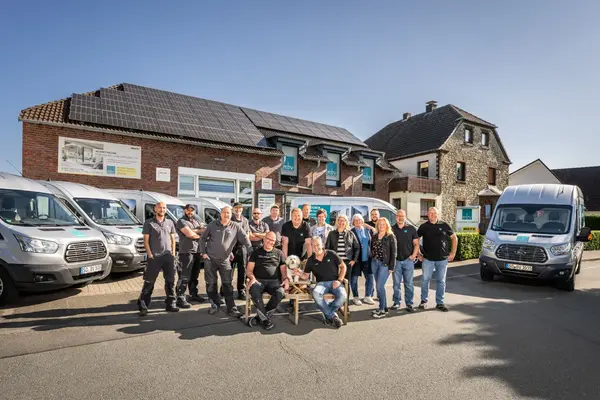 Teamfoto vor Handwerksbetrieb mit Solaranlage und Montagefahrzeugen für Fensterbau