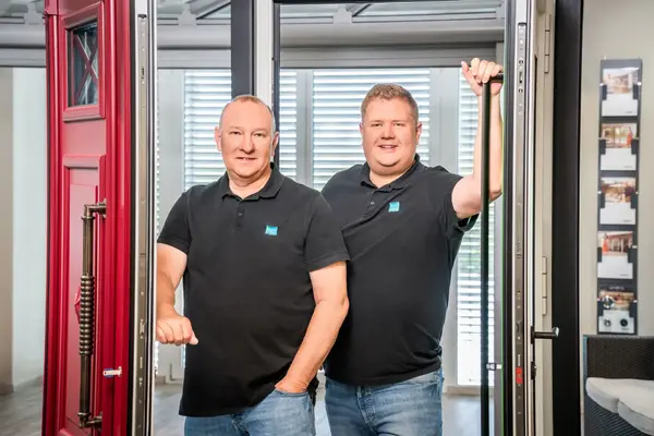 Zwei Fensterbauer im Showroom zeigen Haustür und Fenster mit Griffstange