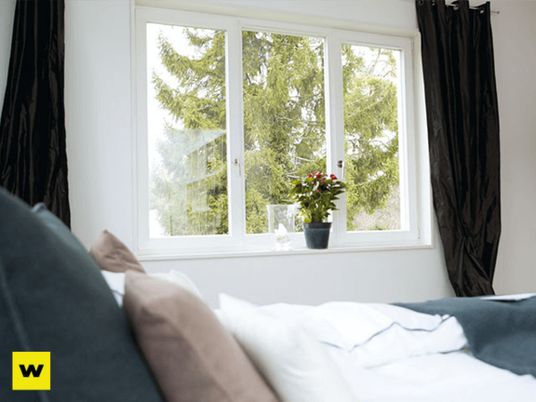 Helles Schlafzimmer mit großem Fenster, Bett und Blumentopf für gemütliches Wohnen.