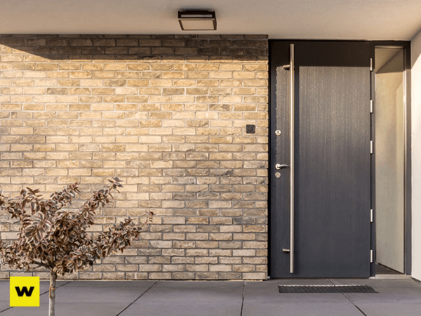 Moderne Haustür aus Aluminium neben heller Klinkerfassade und kleiner Pflanze im Eingangsbereich.