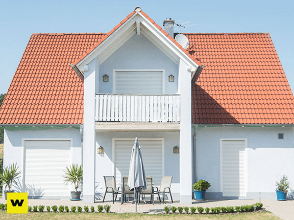 Modernes Einfamilienhaus mit rotem Satteldach, Balkon und Gartenmöbeln im Vorgarten.